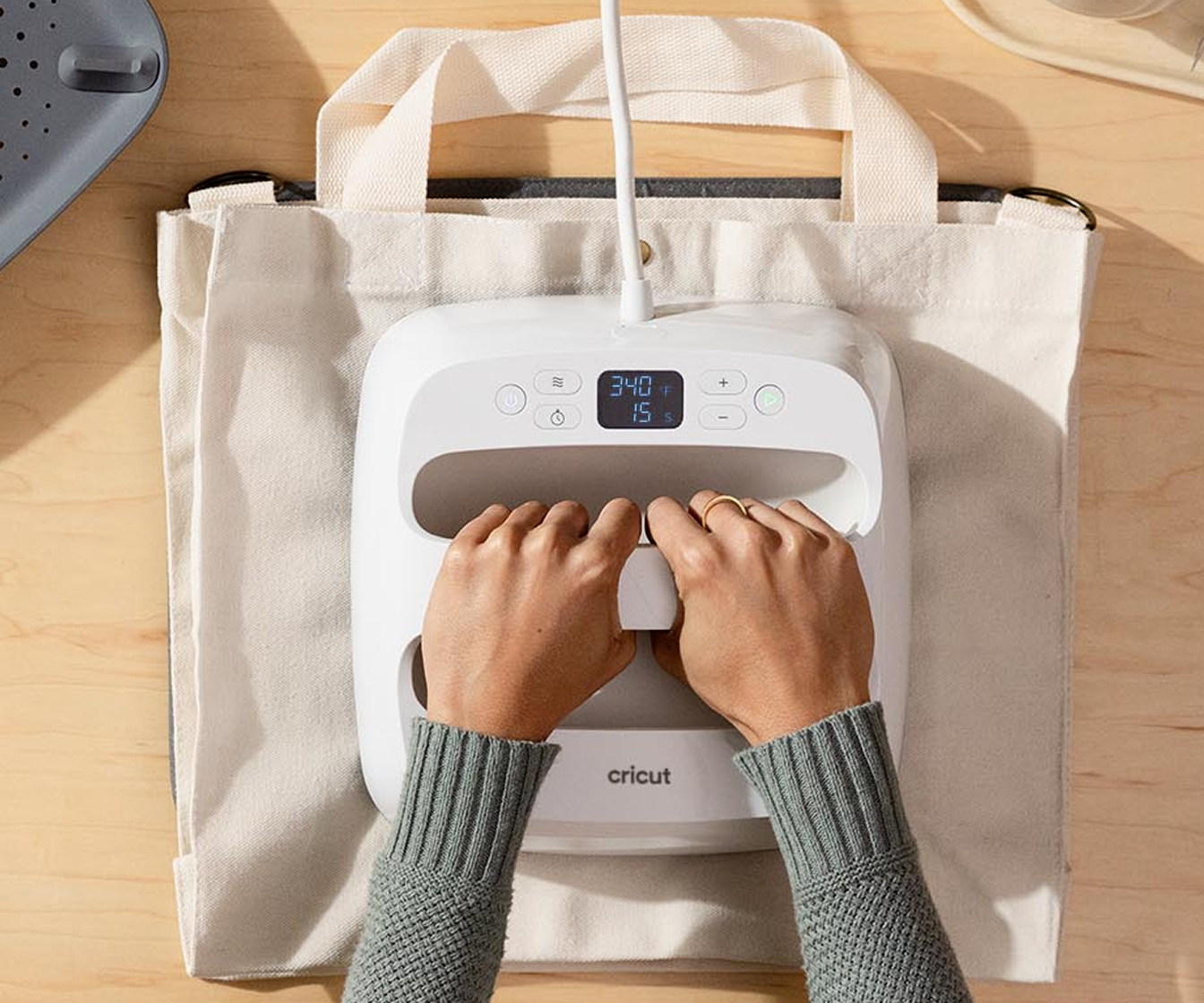 a persons hands using a Cricut Easypress SE to apply design onto a canvas tote bag