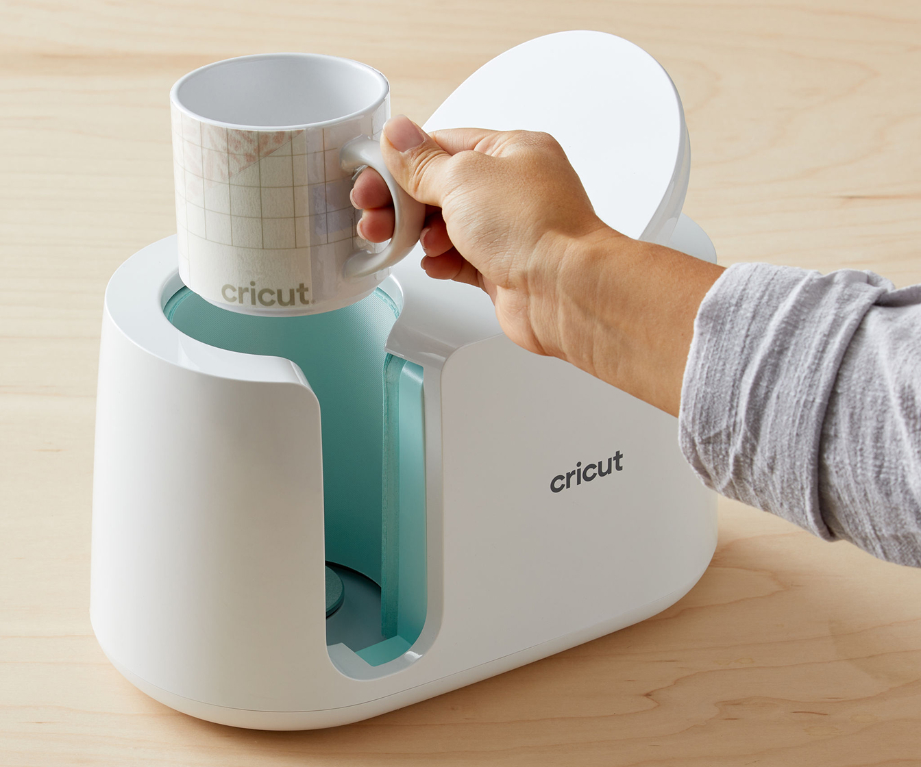 a person's hand taking a printed mug out of a Cricut Mug Press machine.