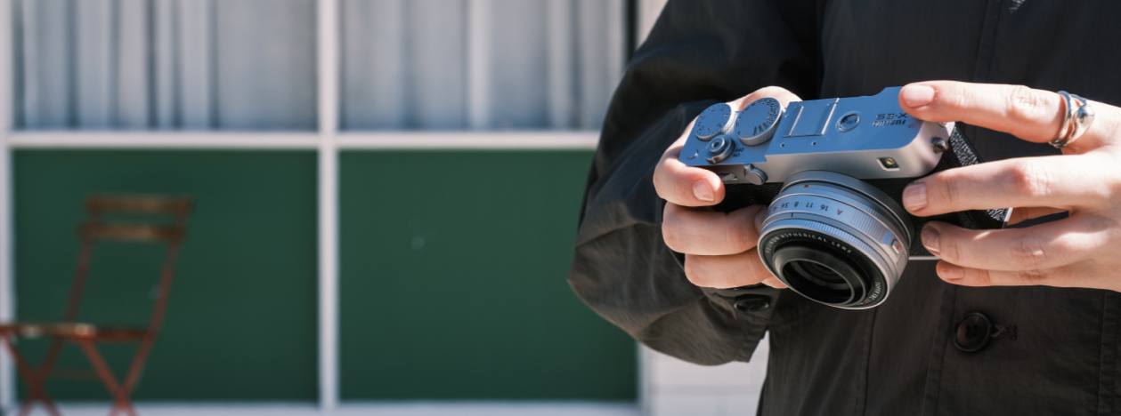 Person holding a Fujifilm X-E3 camera outdoors with focus on the camera body and lens.