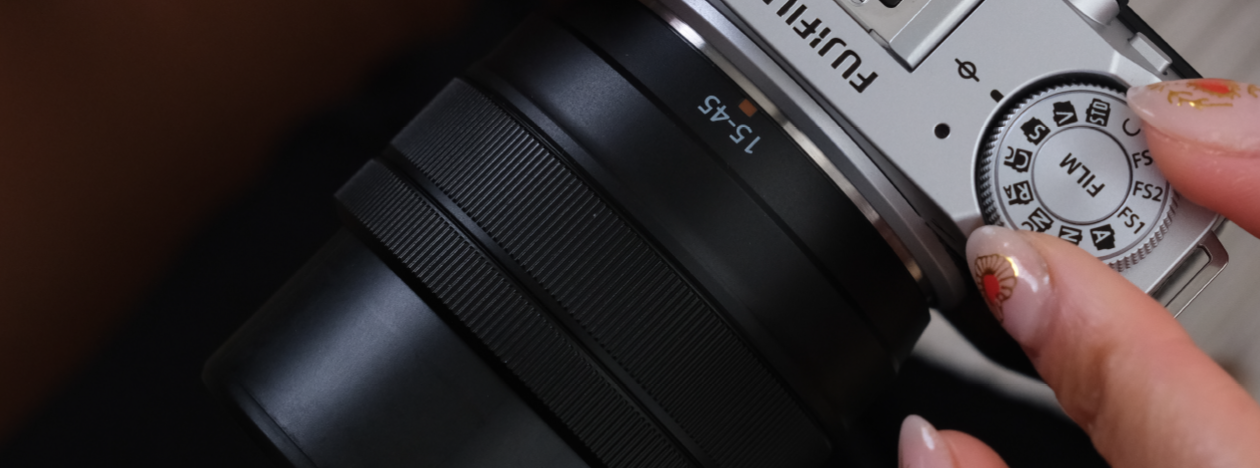 Close-up of a person adjusting the mode dial on a Fujifilm camera with a 15–45mm lens